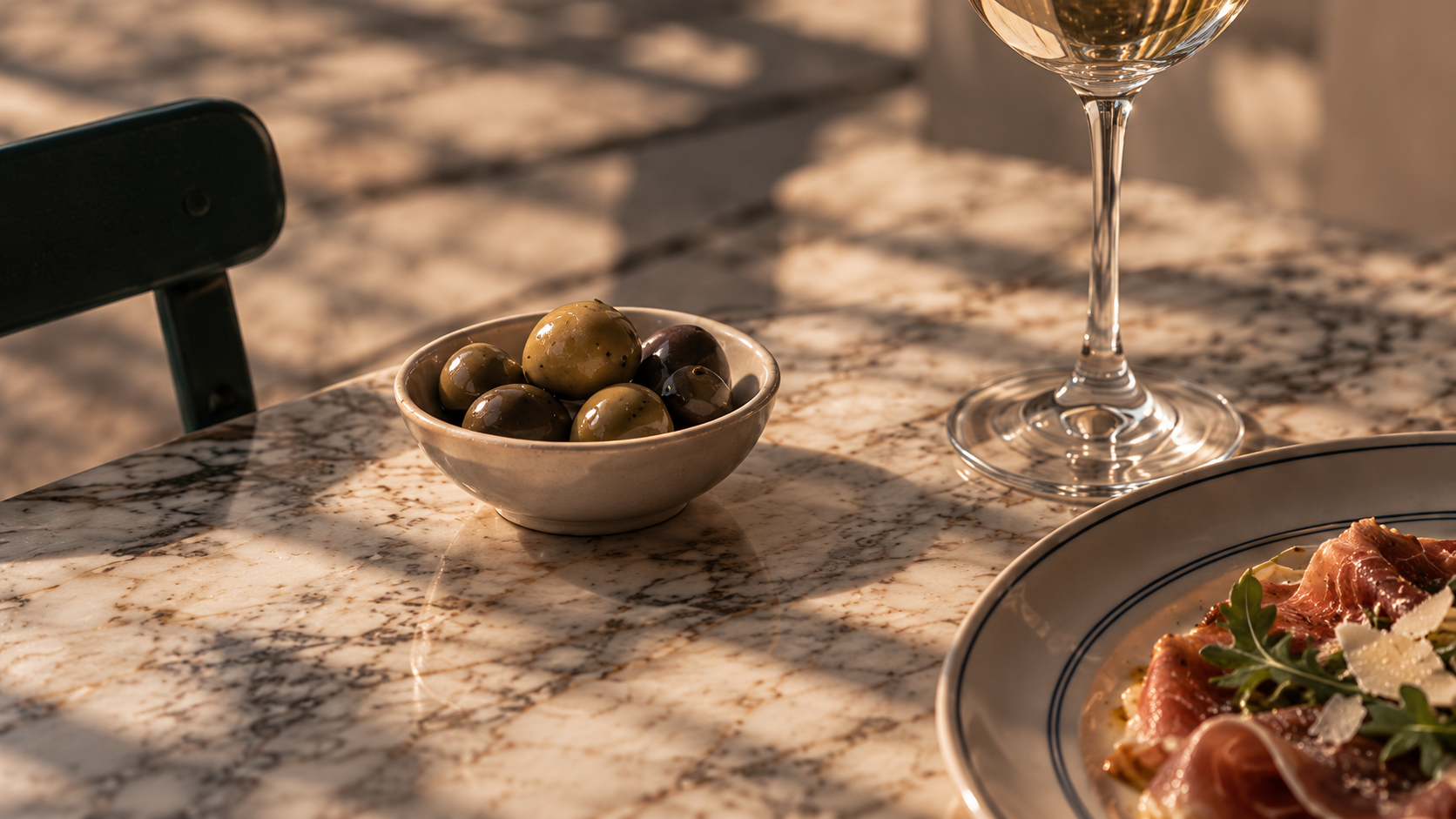 Marble table with olives, a glass of white wine and a plate in the sunlight